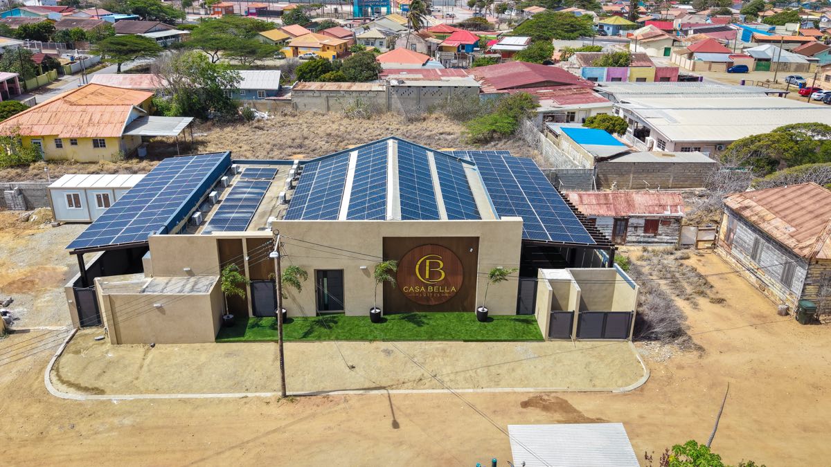 The front of Casabella Suites from the air — the Casa Bella sign on the facade, lawn in front and the solar roof behind.