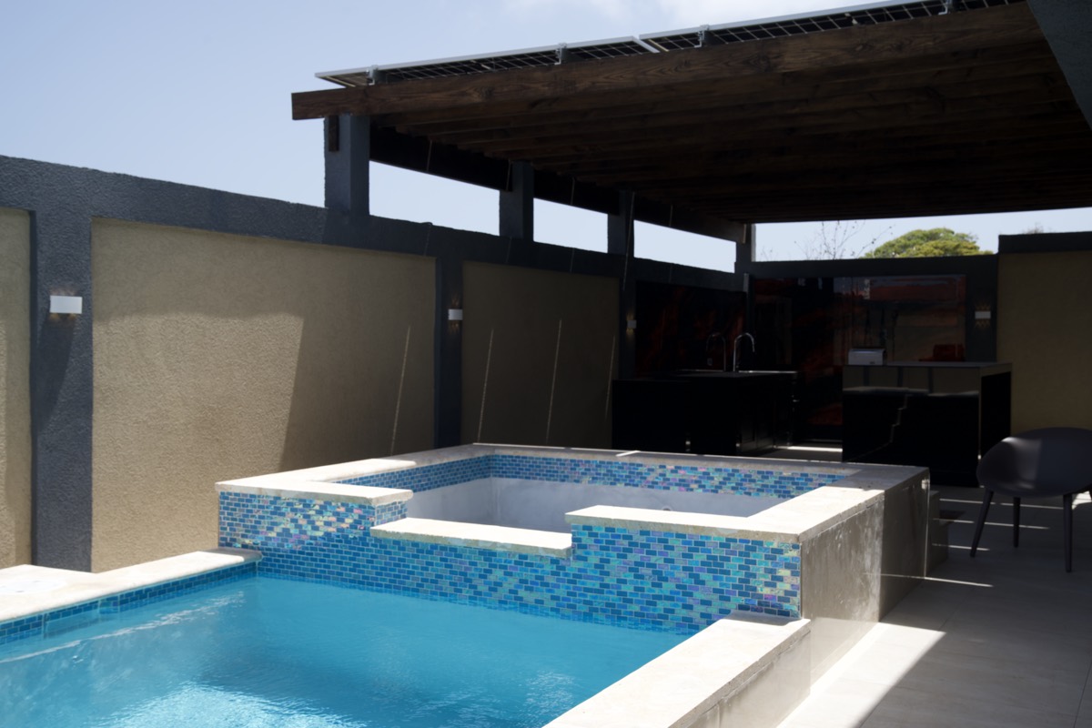 The pool at Casabella Suites, with travertine coping, a spa at the far end and the pergola over the outdoor kitchen.